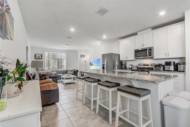 kitchen featuring light stone countertops, white cabinetry, a center island with sink, and appliances with stainless steel finishes