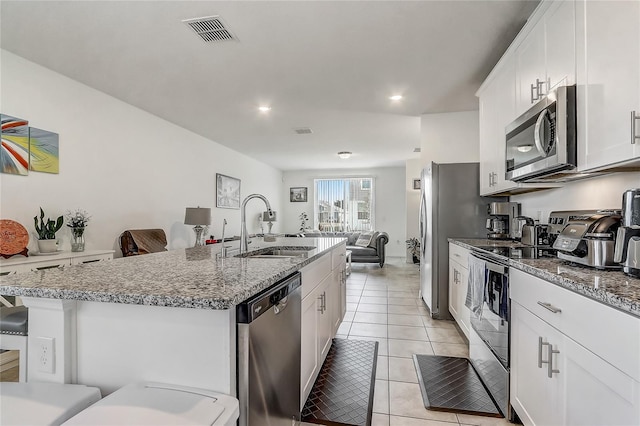 kitchen featuring appliances with stainless steel finishes, white cabinetry, light tile patterned floors, a kitchen bar, and a kitchen island with sink