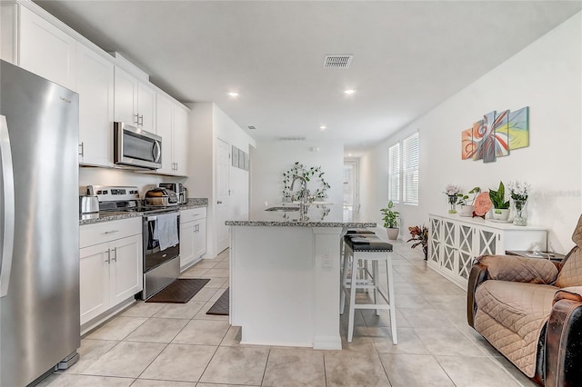 kitchen with white cabinets, stainless steel appliances, an island with sink, a breakfast bar, and stone counters