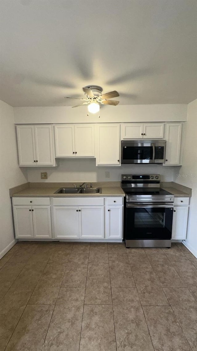 kitchen featuring appliances with stainless steel finishes, white cabinetry, sink, ceiling fan, and light tile patterned floors