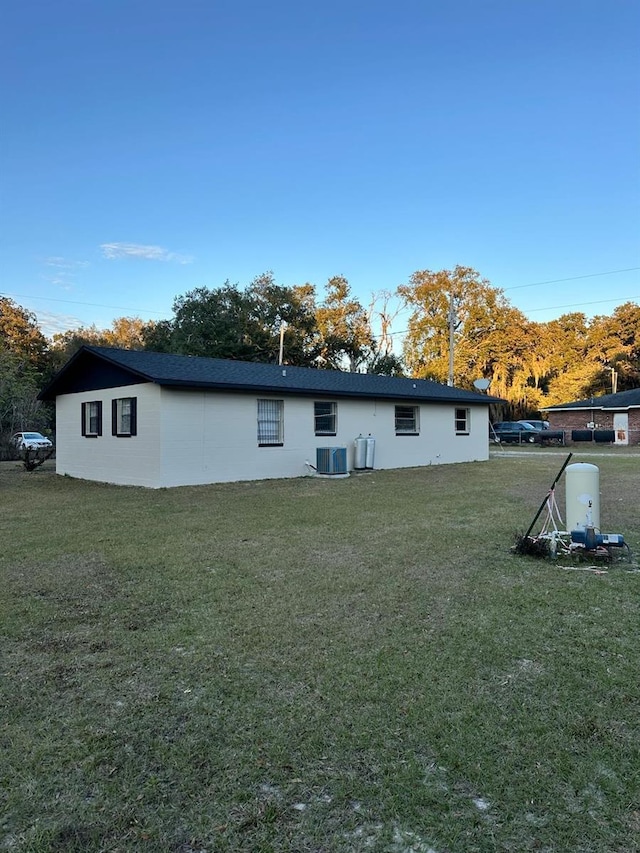 rear view of house with central AC unit and a lawn