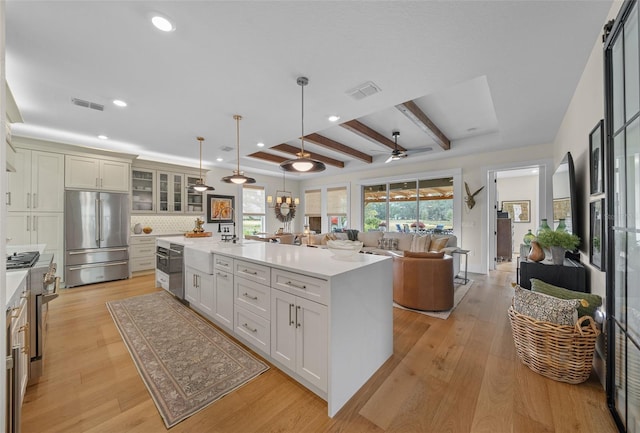 kitchen featuring tasteful backsplash, high end refrigerator, decorative light fixtures, beam ceiling, and a kitchen island with sink