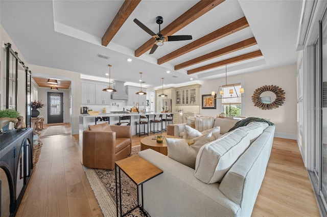 living room with ceiling fan, beam ceiling, a raised ceiling, and light hardwood / wood-style flooring