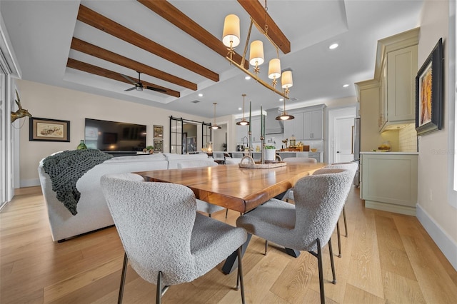 dining room with beamed ceiling, a barn door, ceiling fan with notable chandelier, and light wood-type flooring