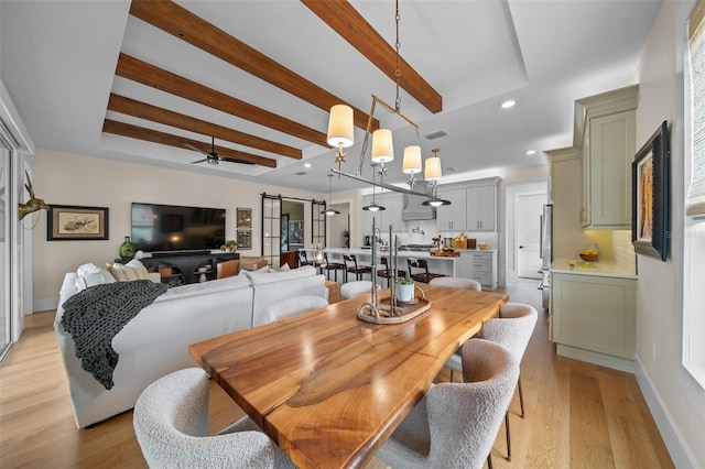 dining space featuring beamed ceiling, ceiling fan, a barn door, and light hardwood / wood-style floors