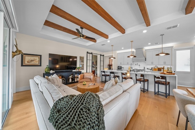 living room with beamed ceiling, ceiling fan, a barn door, and light hardwood / wood-style floors