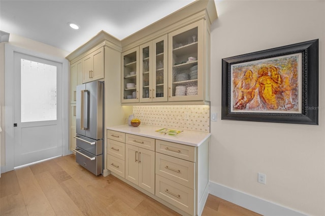 kitchen with tasteful backsplash, cream cabinets, high end refrigerator, and light hardwood / wood-style flooring