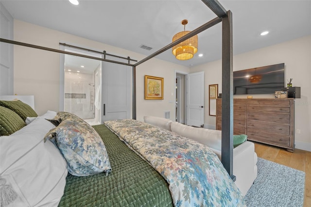 bedroom with a barn door, connected bathroom, and light hardwood / wood-style floors