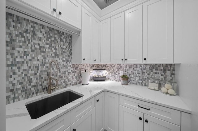 kitchen with light stone countertops, sink, white cabinets, and backsplash