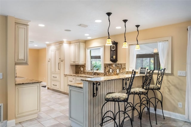 kitchen with stone counters, pendant lighting, kitchen peninsula, and tasteful backsplash