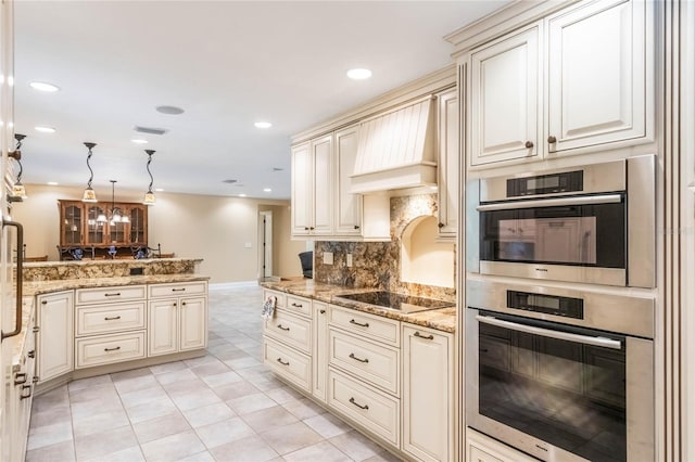 kitchen with kitchen peninsula, light stone countertops, double oven, black electric cooktop, and cream cabinets