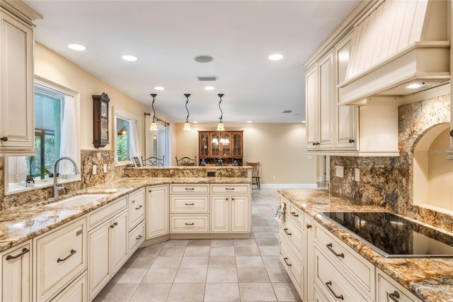 kitchen with premium range hood, kitchen peninsula, hanging light fixtures, cream cabinets, and sink