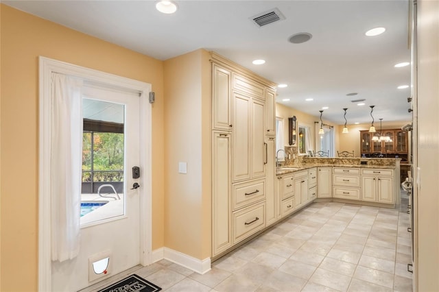 kitchen with kitchen peninsula, sink, hanging light fixtures, light stone countertops, and cream cabinetry