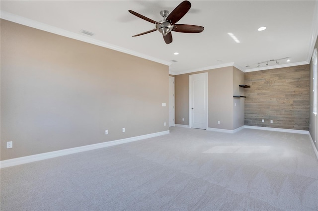 carpeted empty room with crown molding, track lighting, ceiling fan, and wood walls