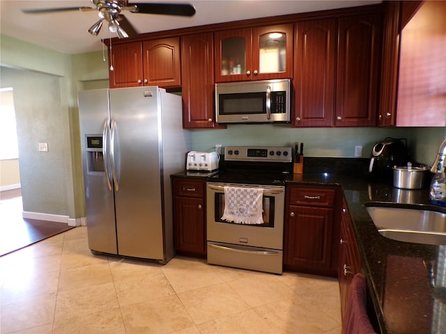 kitchen with stainless steel appliances, dark stone counters, glass insert cabinets, and ceiling fan