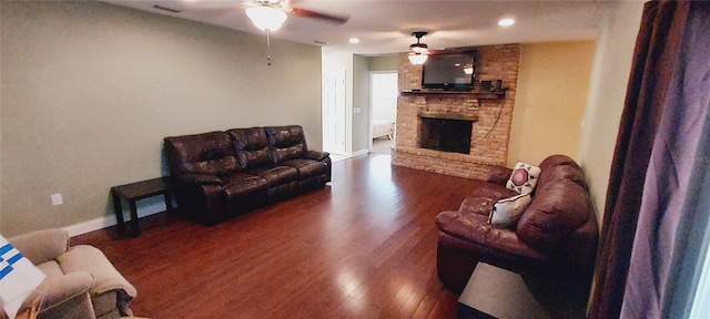 living room with ceiling fan, a stone fireplace, wood finished floors, visible vents, and baseboards