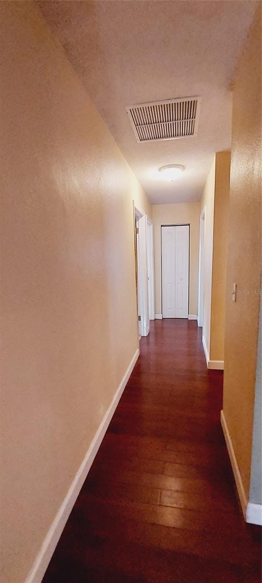 corridor with baseboards, visible vents, and wood finished floors