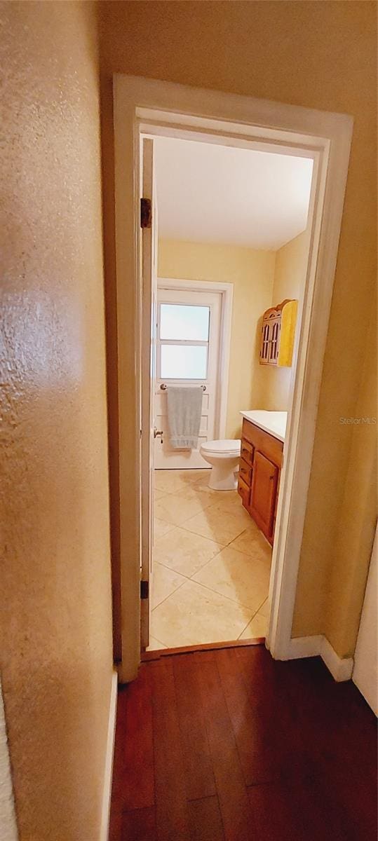 hallway with a textured wall, light wood-type flooring, and baseboards