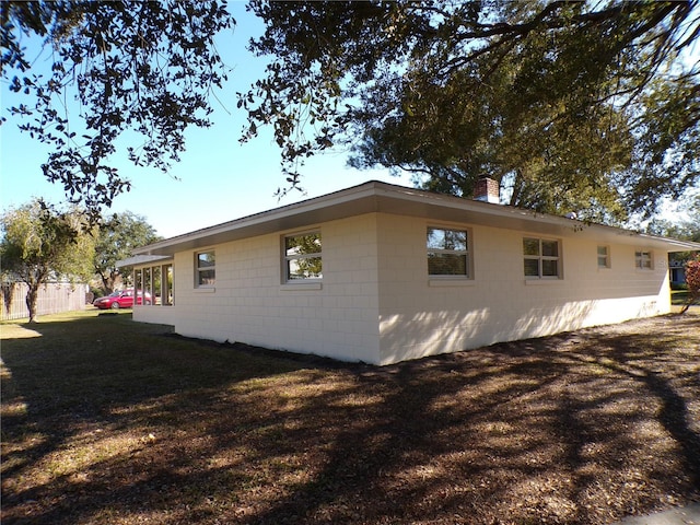 view of side of home with concrete block siding, a yard, and a chimney