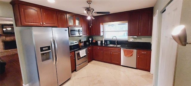 kitchen with ceiling fan, stainless steel appliances, a sink, dark countertops, and glass insert cabinets