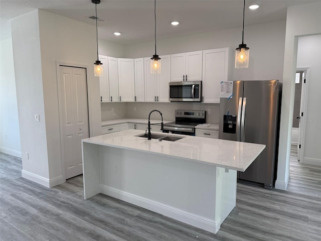 kitchen with light stone countertops, white cabinets, appliances with stainless steel finishes, and a center island with sink