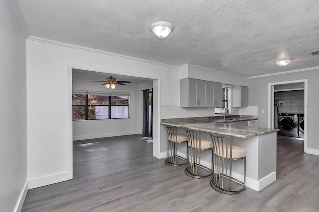 kitchen featuring gray cabinets, a breakfast bar, backsplash, kitchen peninsula, and washer and clothes dryer