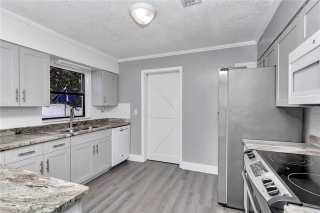 kitchen with sink, white appliances, backsplash, light stone countertops, and light wood-type flooring