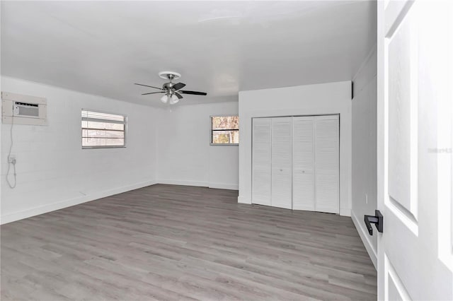 unfurnished bedroom with multiple windows, hardwood / wood-style flooring, a wall unit AC, and ceiling fan