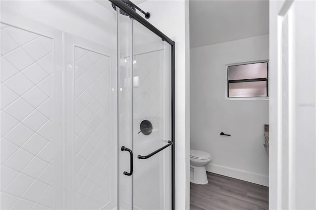 bathroom with hardwood / wood-style floors, a shower with shower door, and toilet