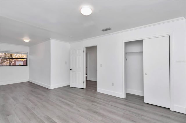 unfurnished bedroom featuring light hardwood / wood-style flooring, ornamental molding, and a closet