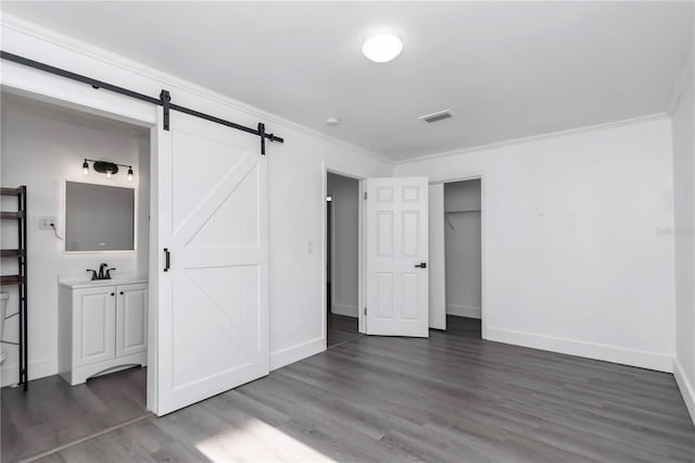 unfurnished bedroom with crown molding, a barn door, dark hardwood / wood-style flooring, and sink