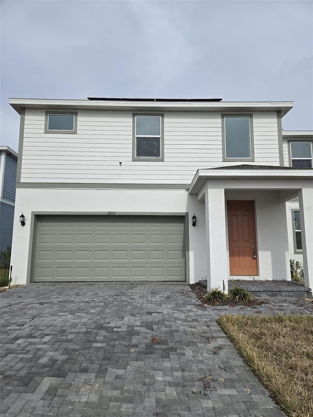 traditional-style house featuring a garage, decorative driveway, and stucco siding