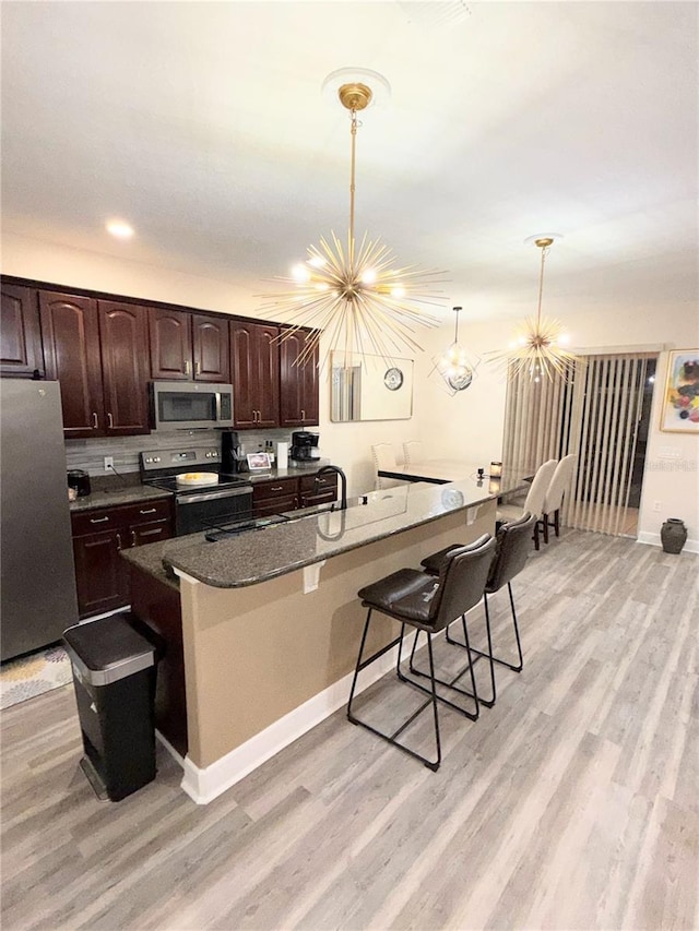 kitchen featuring an inviting chandelier, hanging light fixtures, a kitchen breakfast bar, stainless steel appliances, and dark brown cabinets