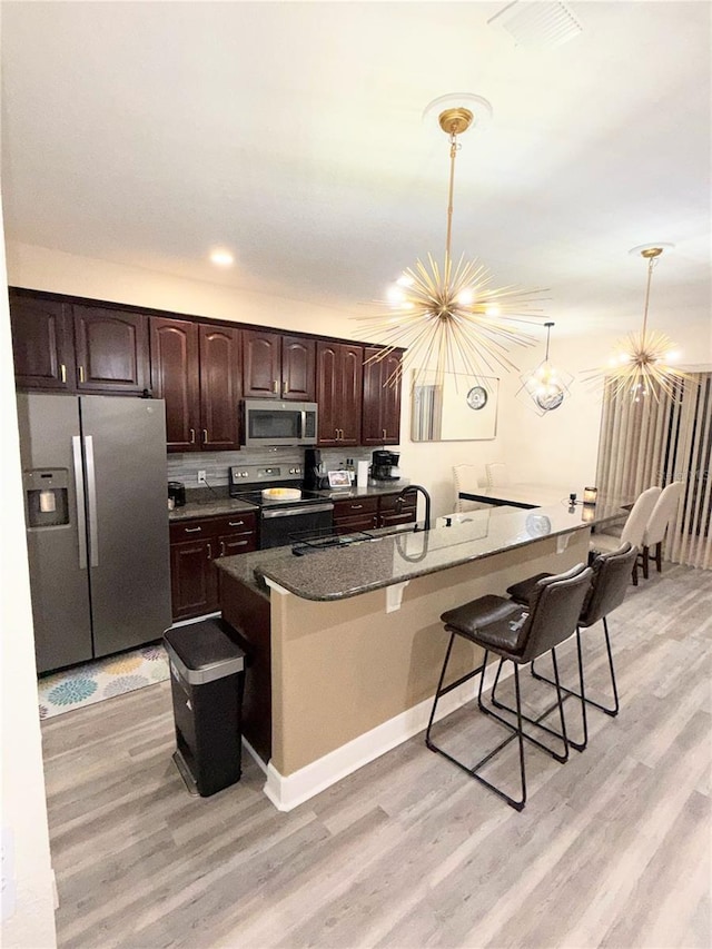 kitchen featuring decorative light fixtures, a kitchen bar, an inviting chandelier, appliances with stainless steel finishes, and dark brown cabinets