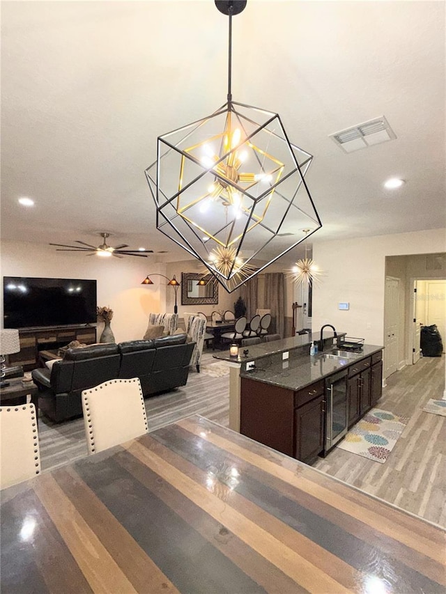 dining area featuring light hardwood / wood-style floors, ceiling fan with notable chandelier, beverage cooler, and sink