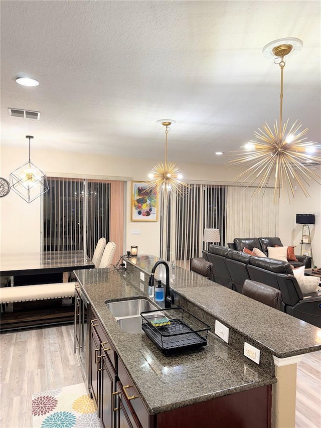 kitchen with decorative light fixtures, dark stone countertops, sink, a chandelier, and dark brown cabinets