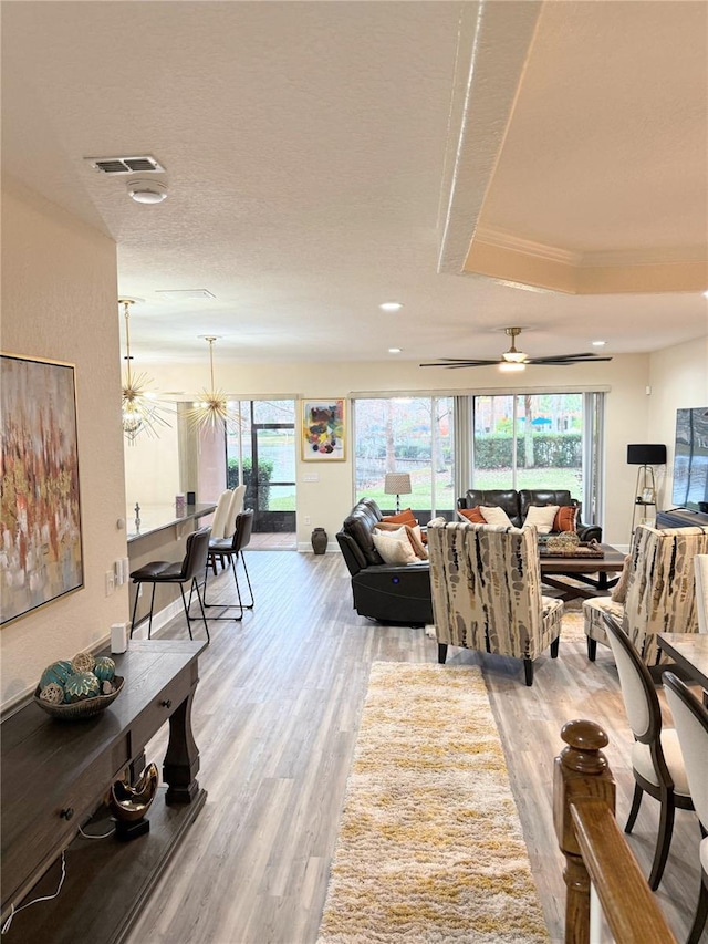 living room featuring a raised ceiling, ceiling fan, crown molding, and light hardwood / wood-style floors