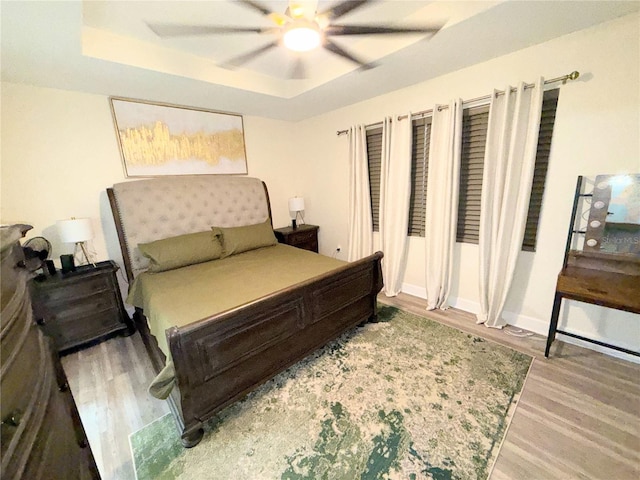 bedroom featuring a raised ceiling, ceiling fan, and light wood-type flooring