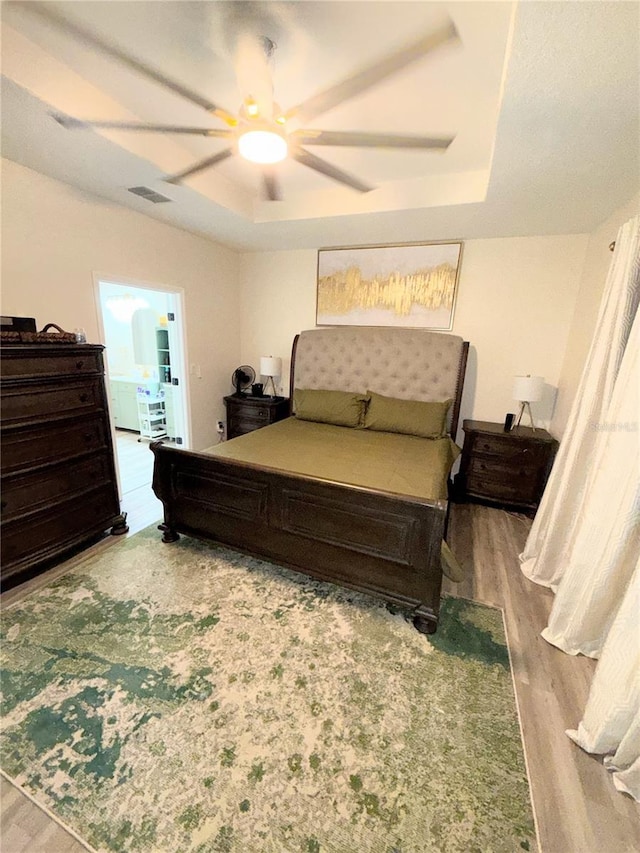 bedroom featuring ceiling fan, light hardwood / wood-style floors, and a tray ceiling