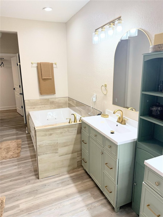 bathroom with a relaxing tiled tub, wood-type flooring, and vanity