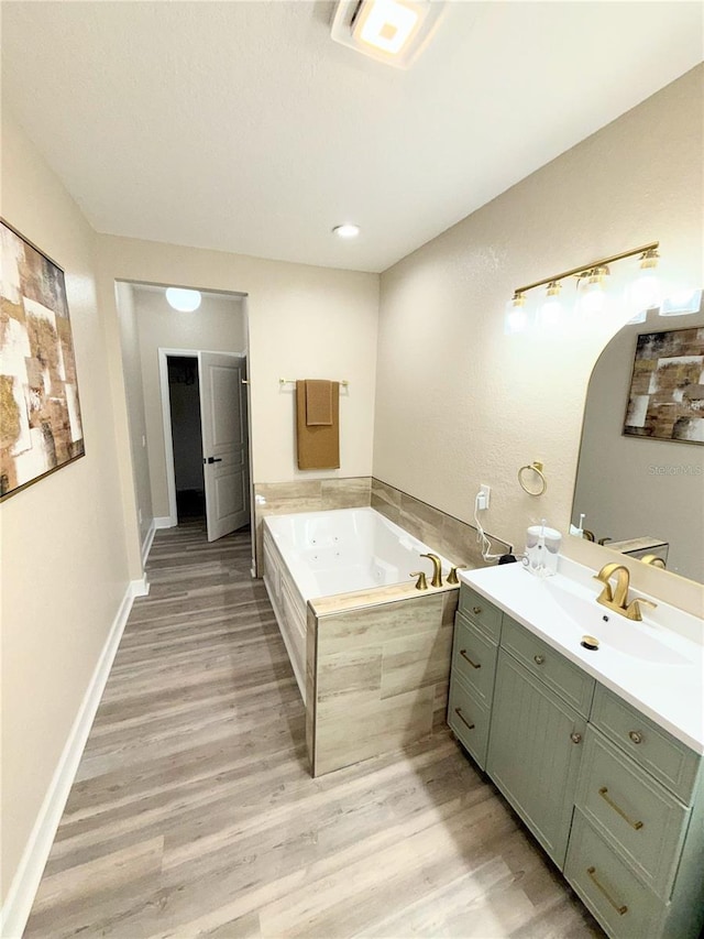 bathroom with hardwood / wood-style flooring, tiled tub, and vanity