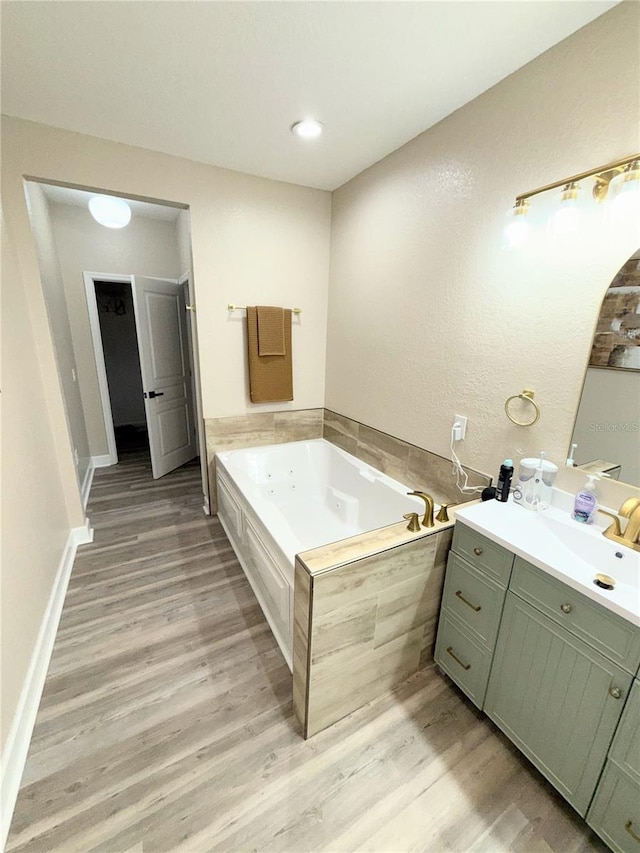 bathroom featuring a relaxing tiled tub, hardwood / wood-style floors, and vanity