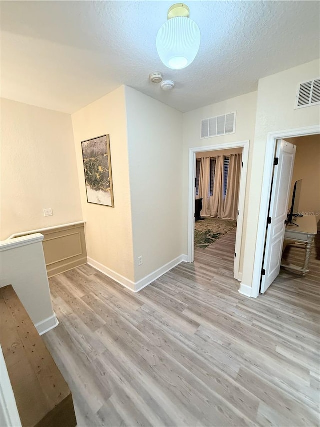 hallway with light wood-type flooring and a textured ceiling