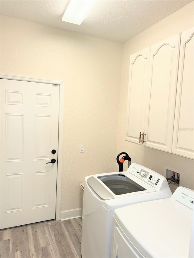 laundry room with light wood-type flooring, washing machine and dryer, a textured ceiling, and cabinets