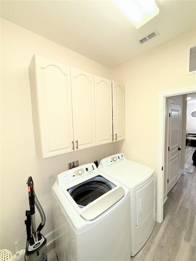 washroom with light wood-type flooring, washer and dryer, and cabinets