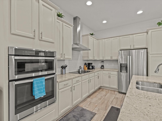 kitchen featuring wall chimney range hood, light stone countertops, sink, and appliances with stainless steel finishes