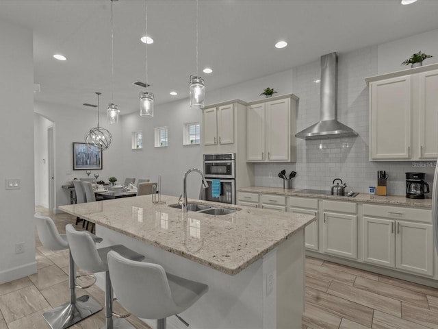 kitchen featuring a center island with sink, pendant lighting, sink, and wall chimney range hood