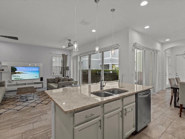 kitchen with sink, hanging light fixtures, a kitchen island with sink, stainless steel dishwasher, and light stone counters