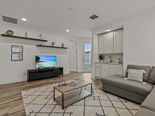 living room featuring wet bar, light hardwood / wood-style flooring, and ornamental molding