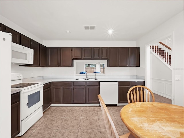 kitchen with light tile patterned floors, dark brown cabinets, sink, and white appliances